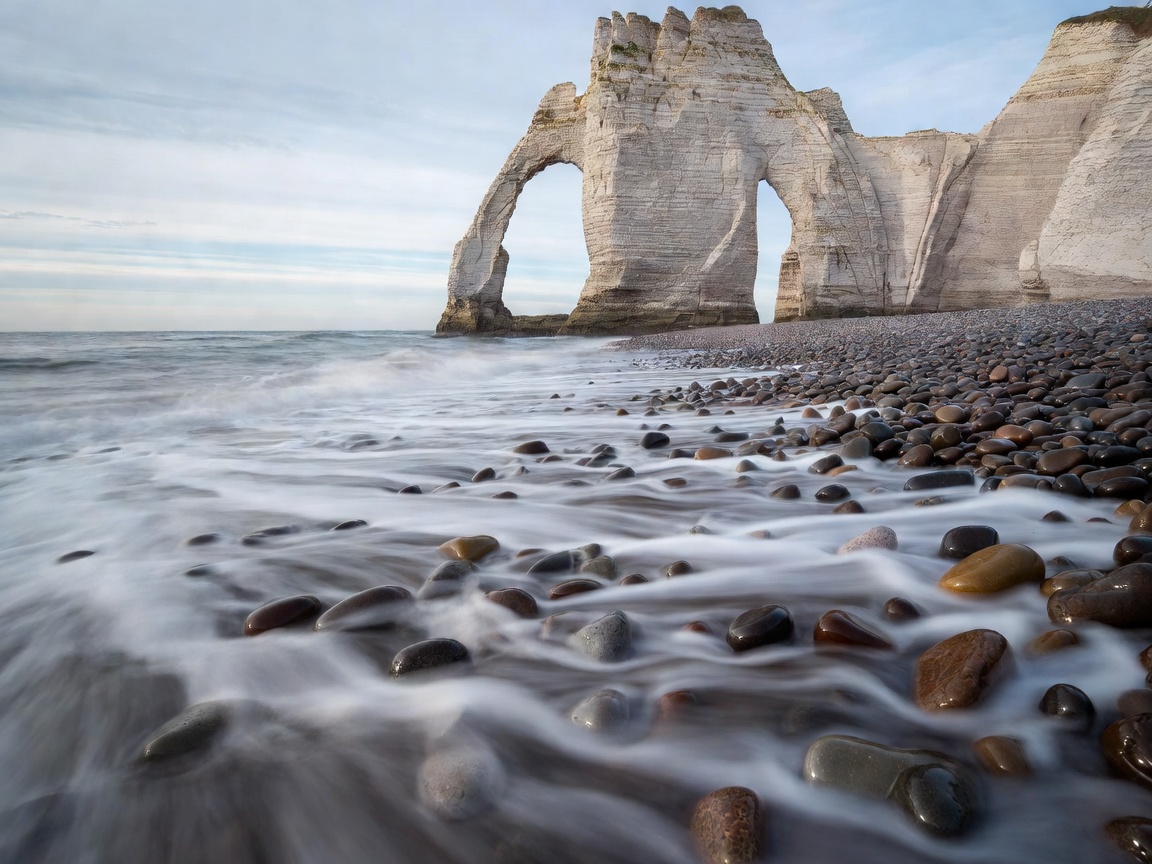 Soft streaks of retreating water around pebbles below the chalk arch at Étretat in Normandy